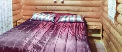 Une pièce de style cabane en bois, avec un lit, des oreillers et une petite table de chevet en bois.