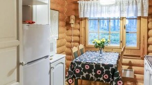 L’intérieur d’un chalet confortable, avec une table à manger dressée pour deux personnes, un réfrigérateur et une fenêtre agrémentée de rideaux.