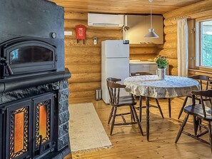 Een gezellig chaletinterieur met een houtkachel, een eettafel met stoelen, een koelkast en een raam met gordijnen.