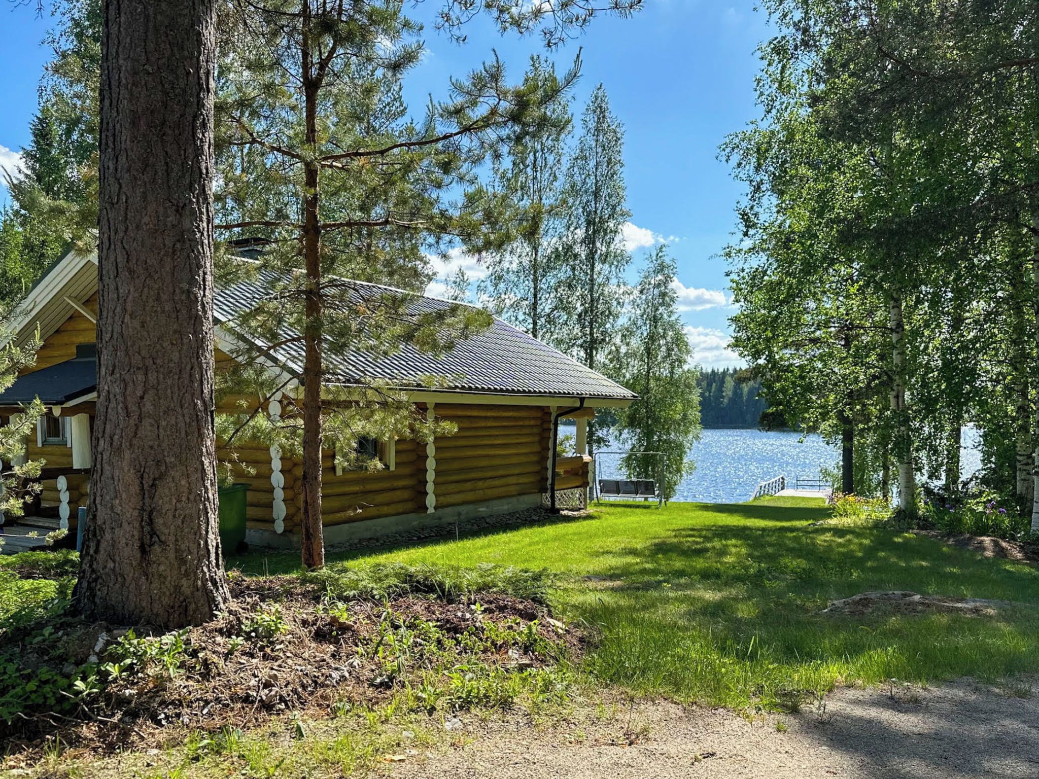 A log cabin with a deck, surrounded by trees and a lake.