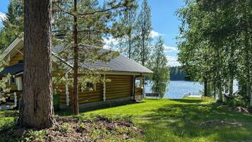 A log cabin with a deck, surrounded by trees and a lake.