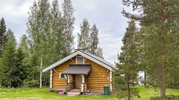 A log cabin with a front porch, surrounded by trees.