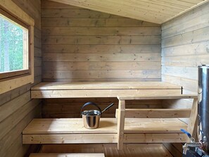 A wooden cabin interior with a window, a metal bucket, and a water tap.
