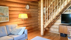 A cozy log cabin interior with a sofa, ottoman, wooden staircase, and a television. - Suviranta by Interhome (Lapinlahti)