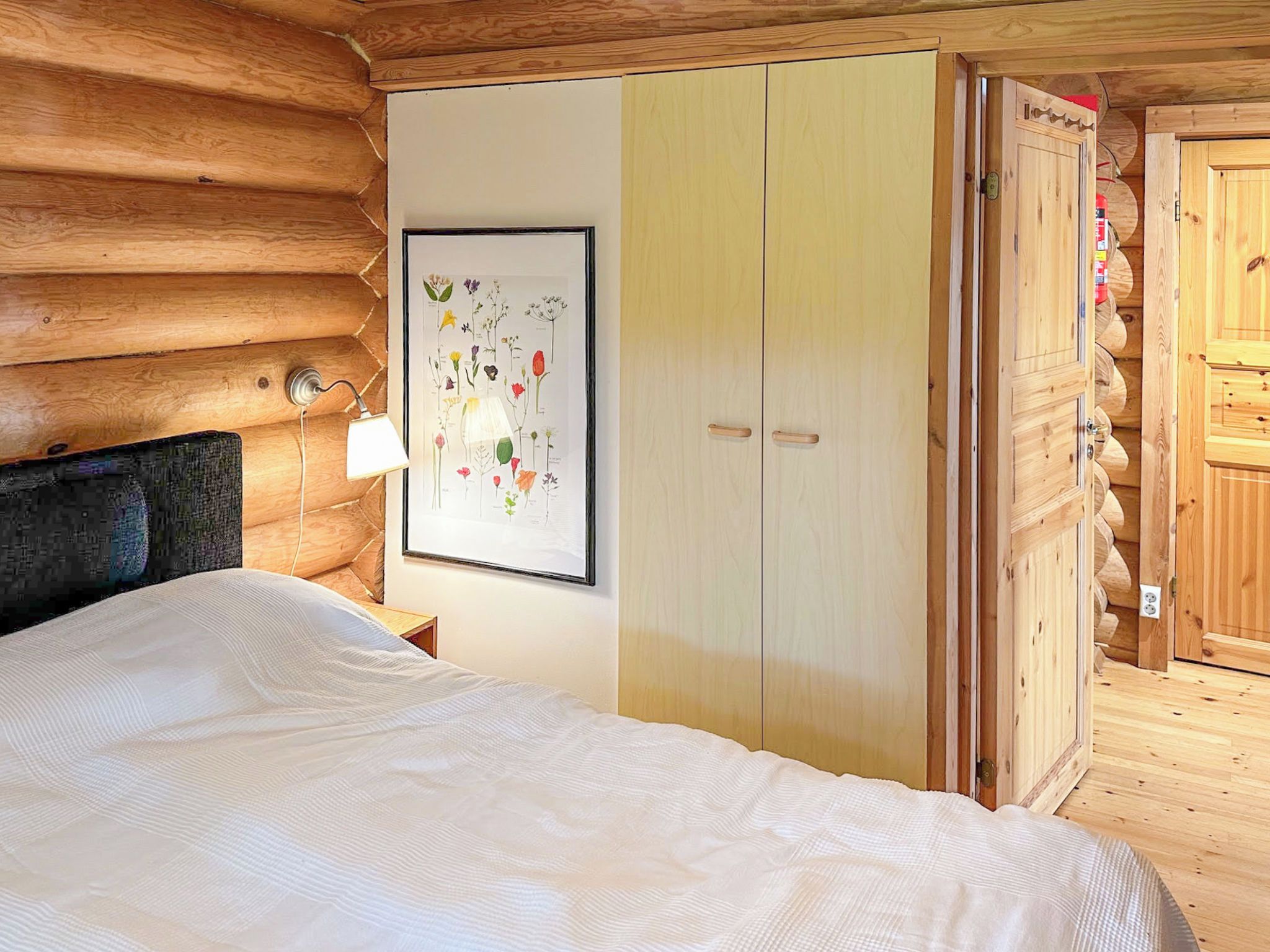 A wooden cabin room with a bed, a wardrobe, and a framed botanical illustration on the wall.