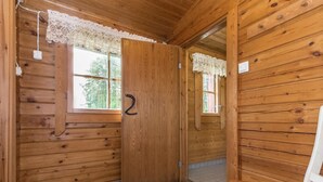 L’intérieur d’une cabane en bois, avec une seule porte, une fenêtre et une chaise en bois.