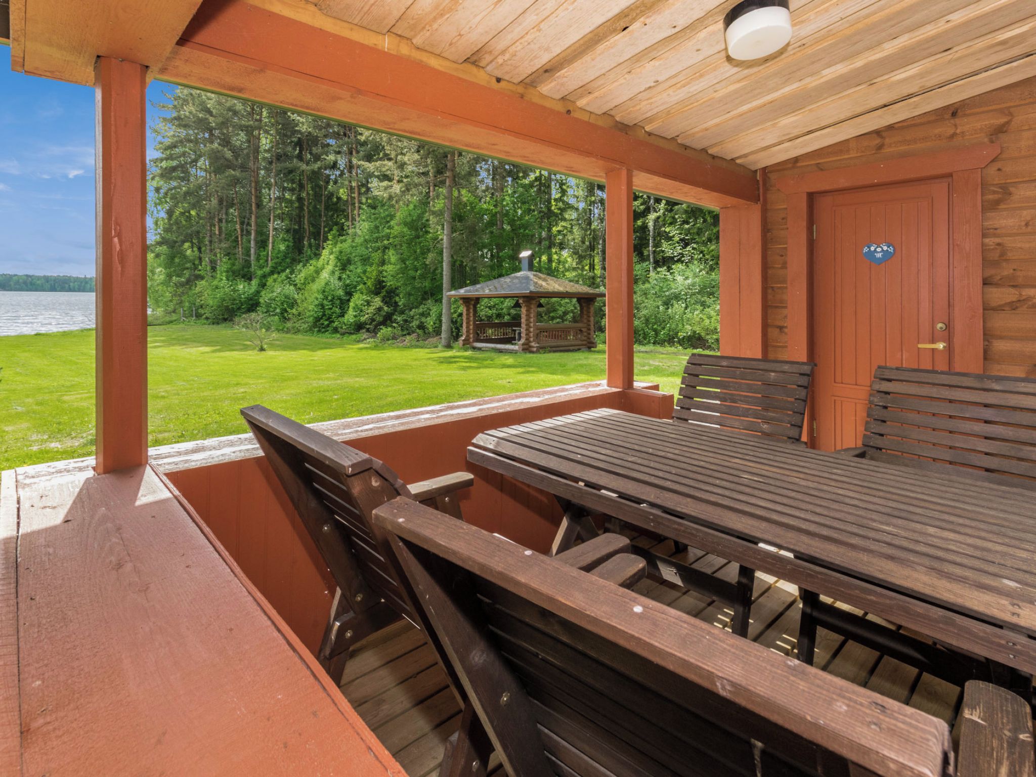 A covered outdoor area with a wooden table and benches, a gazebo, and a view of a lake and forest.