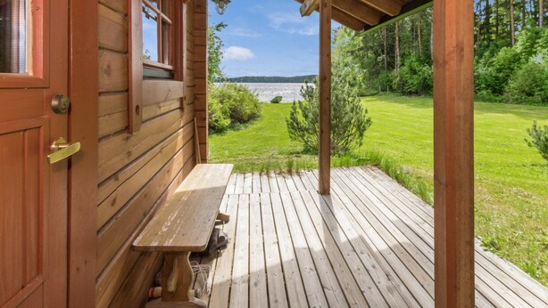 Une cabane en bois avec une véranda, un banc et une vue sur un lac.