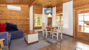 L’intérieur chaleureux d’un chalet avec un plafond en bois, un coin repas comprenant une table et des chaises, un canapé avec des coussins et un téléviseur fixé au mur.
