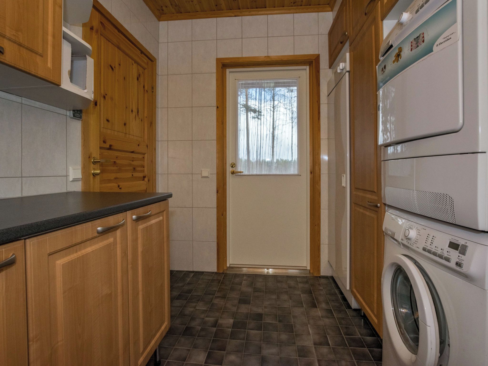 Una cucina compatta con mobili in legno, un forno a microonde integrato e una lavatrice.