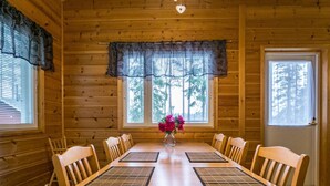 A wooden cabin dining room with a large table, chairs, and a vase of flowers. - Metsäpirtti by Interhome (Parkano)