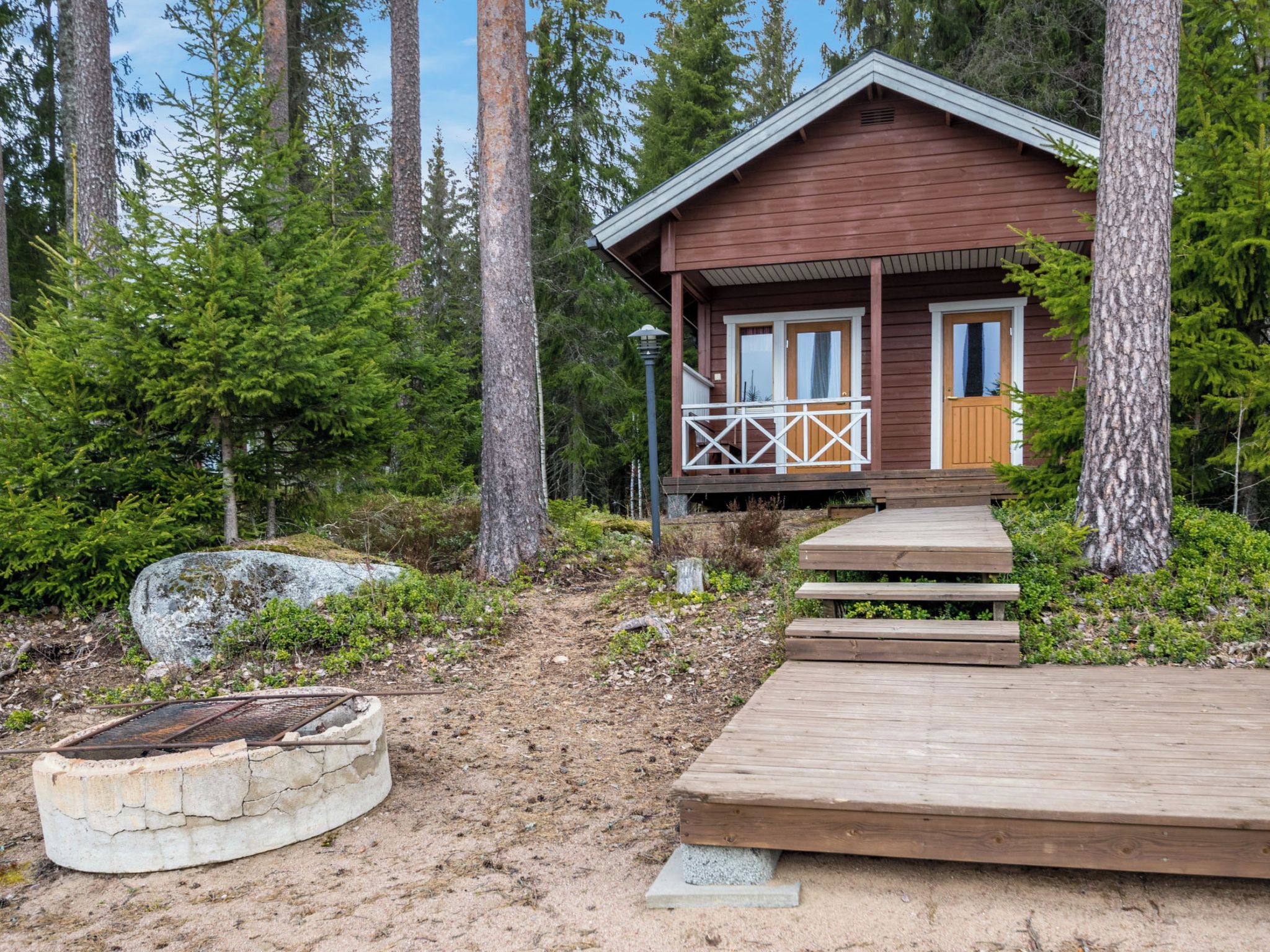 Eine Holzhütte mit Veranda und Stufen zum Eingang, umgeben von Bäumen und einem Feldweg.