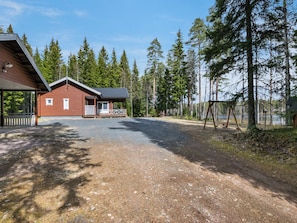 A cabin with a covered porch and a fenced-in area with a swing set. - Metsäpirtti by Interhome (Parkano)