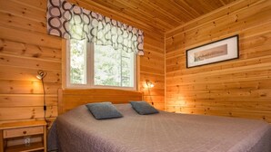 A wooden cabin room with a bed, two pillows, a nightstand, a lamp, and a window with blinds. - Metsäpirtti by Interhome (Parkano)
