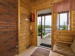 Interno di una baita in legno con un estintore, una scopa e vista su un lago attraverso una finestra.