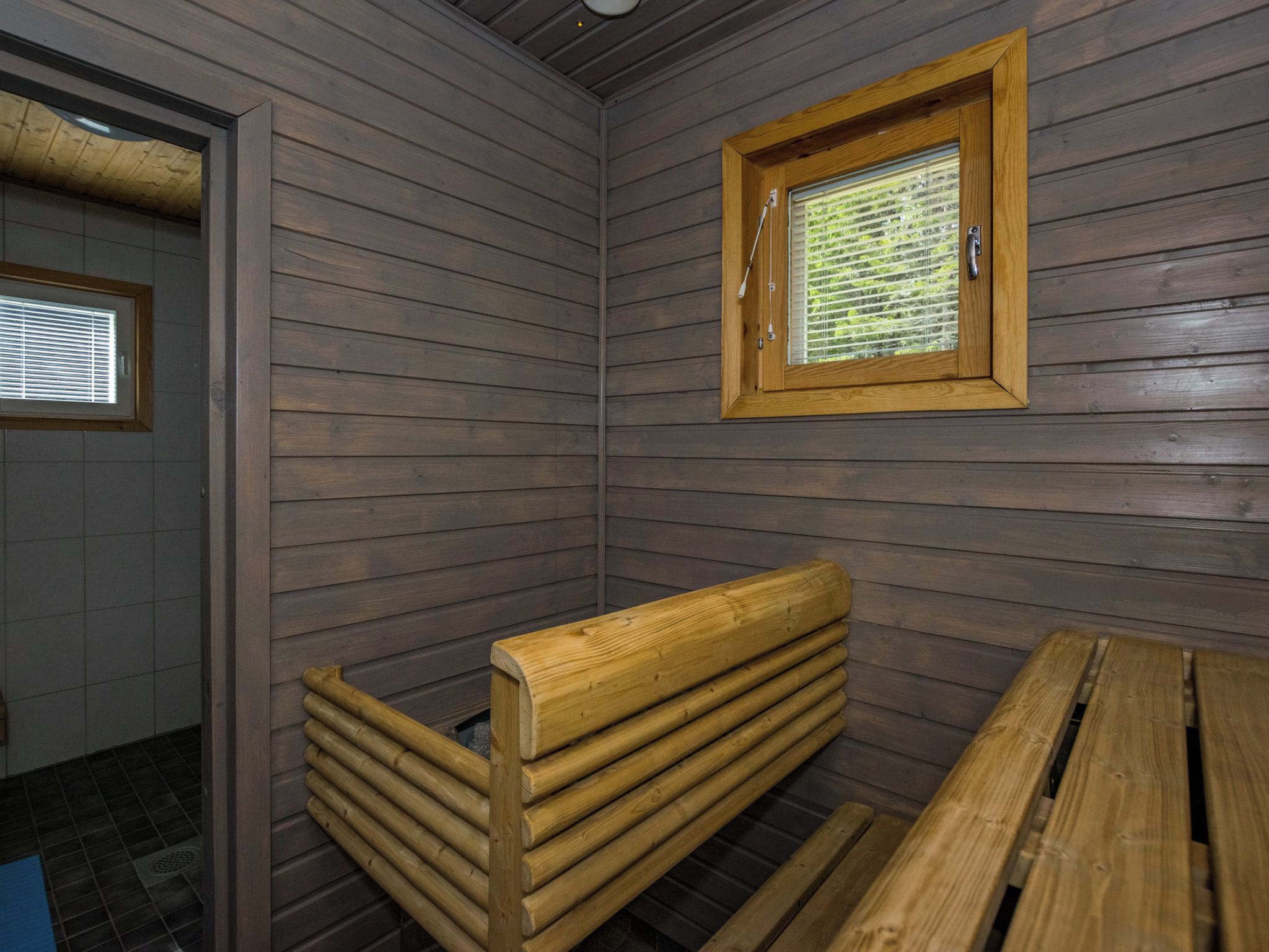 A sauna room with wooden benches and a window with blinds.