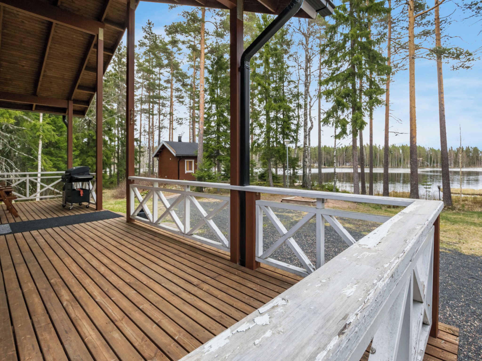 Een houten terras met een balustrade, een klein gebouw en een meer op de achtergrond.