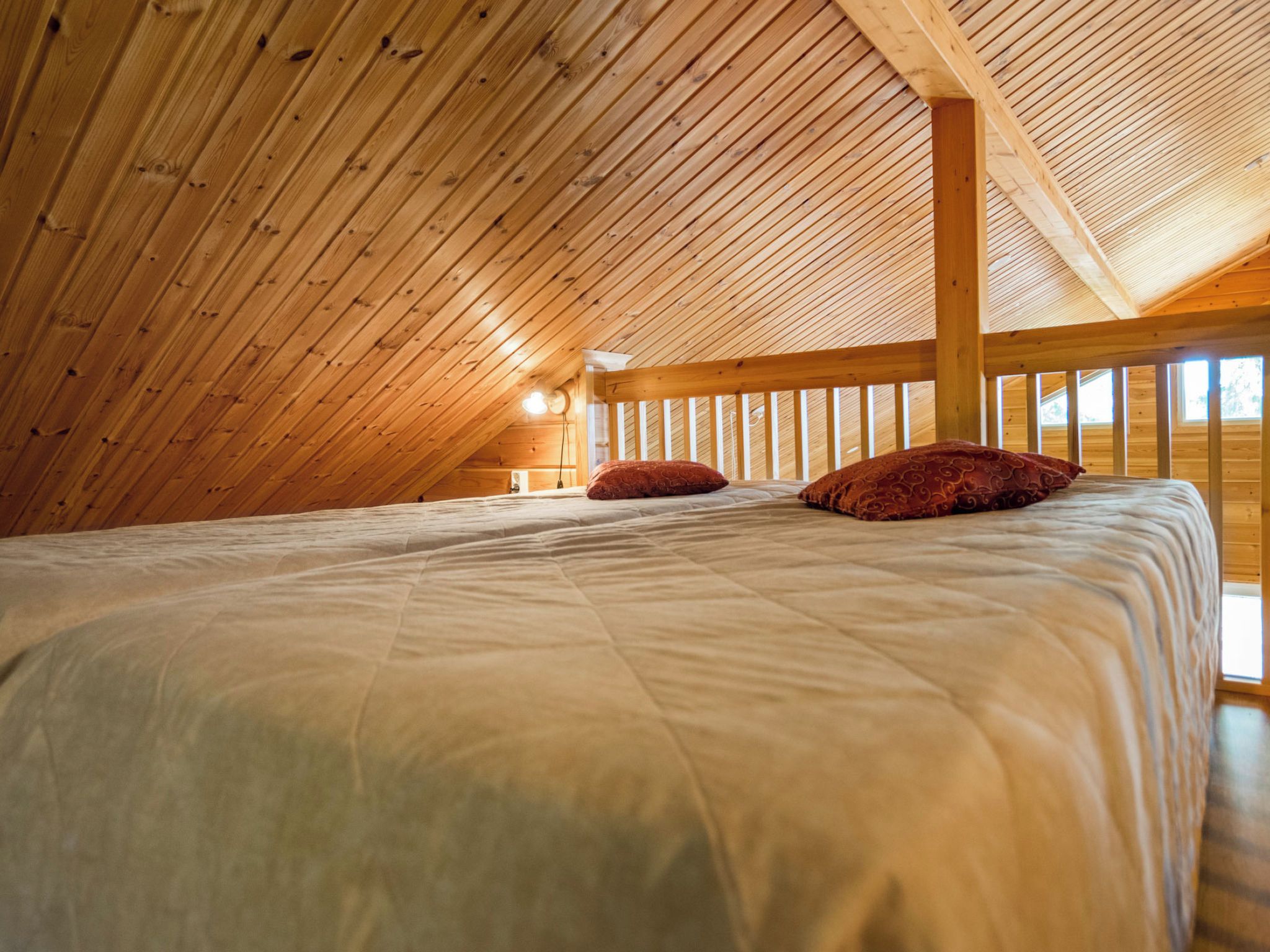 Ein Zimmer mit hohen Decken und einem Holzdach, ein Bett mit weißer Bettwäsche und zwei roten Kissen, sowie ein Fenster, das natürliches Licht hereinlässt.