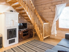 Een houten interieur met een trap, een open haard, een televisie en een bank.