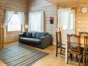 L’intérieur d’un chalet chaleureux, avec un canapé, des fauteuils, un tapis et des murs en bois.