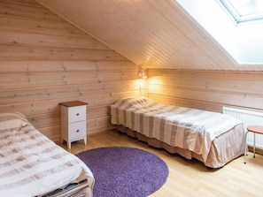 Een knus kamertje met houten wanden en een schuine kap, met een bed, nachtkastje, dressoir en een raam met uitzicht.