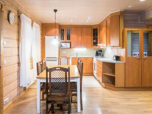 Een kleine keuken met houten kastjes, een eettafel met stoelen, een koelkast en een magnetron.