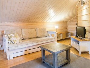 A cozy loft-style room with a wooden ceiling, a sofa with patterned cushions, a small wooden table, and a television on a stand. - Klz 11. jade by Interhome (Sotkamo)