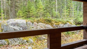 A wooden deck with a railing overlooking a forested area with rocks and trees. - Klz 11. jade by Interhome (Sotkamo)