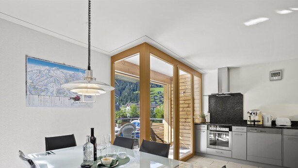 A modern kitchen with a dining area, featuring a large window with a mountain view, a pendant light, and a kitchen island with seating. - Hemmadi by Interhome (Churwalden)