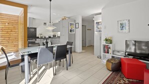 A modern kitchen with white cabinets, a dining area with a glass table, and a living room with a red sofa and a TV. - Hemmadi by Interhome (Churwalden)