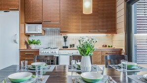 Une cuisine moderne avec des meubles en bois, une cuisinière et un coin repas aménagé pour quatre personnes, avec des assiettes vertes et des verres transparents.