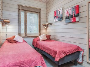 A room with two beds, wooden walls, a window with blinds, and wall-mounted artwork.