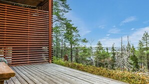 Une terrasse en bois avec un banc, donnant sur une zone boisée et un plan d’eau.