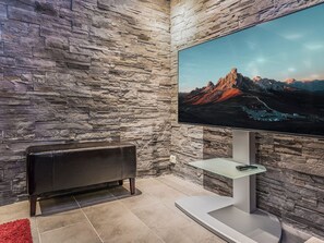 A modern living room with a stone wall, a flat-screen TV mounted on a stand, a leather sofa, and a red rug. - Masto 4 by Interhome (Kuusamo)