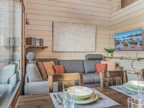 A cozy living room with a wooden floor, a gray sofa with cushions, a wooden dining table set with plates, glasses, and cutlery.