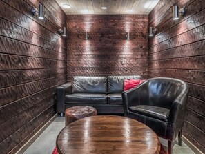 A room with a dark wooden wall, a black leather sofa, a wooden table, and a red pillow. - Masto 4 by Interhome (Kuusamo)