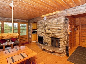 L’intérieur chaleureux d’un chalet avec une cheminée en pierre, des meubles en bois et une grande fenêtre donnant sur le paysage extérieur.