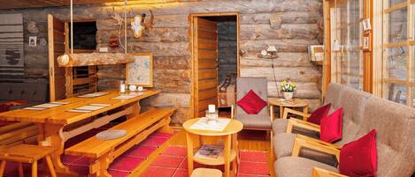 Interior de una cabaña de troncos con comedor, sofá y chimenea.