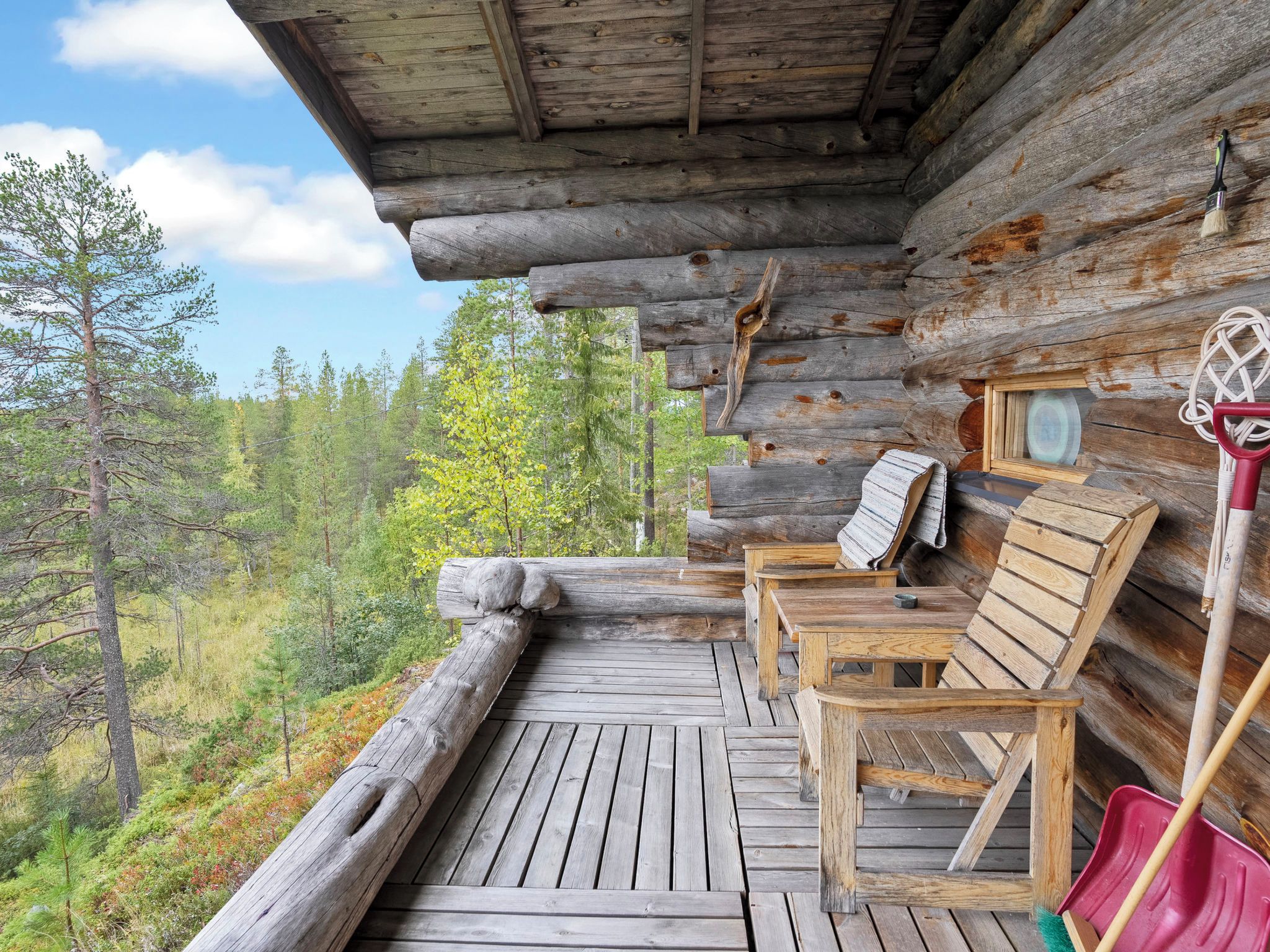 A log cabin with a wooden deck, outdoor seating, and a view of the forest.