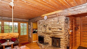 A cozy cabin interior with a stone fireplace, wooden walls, and a dining area with a table and chairs.