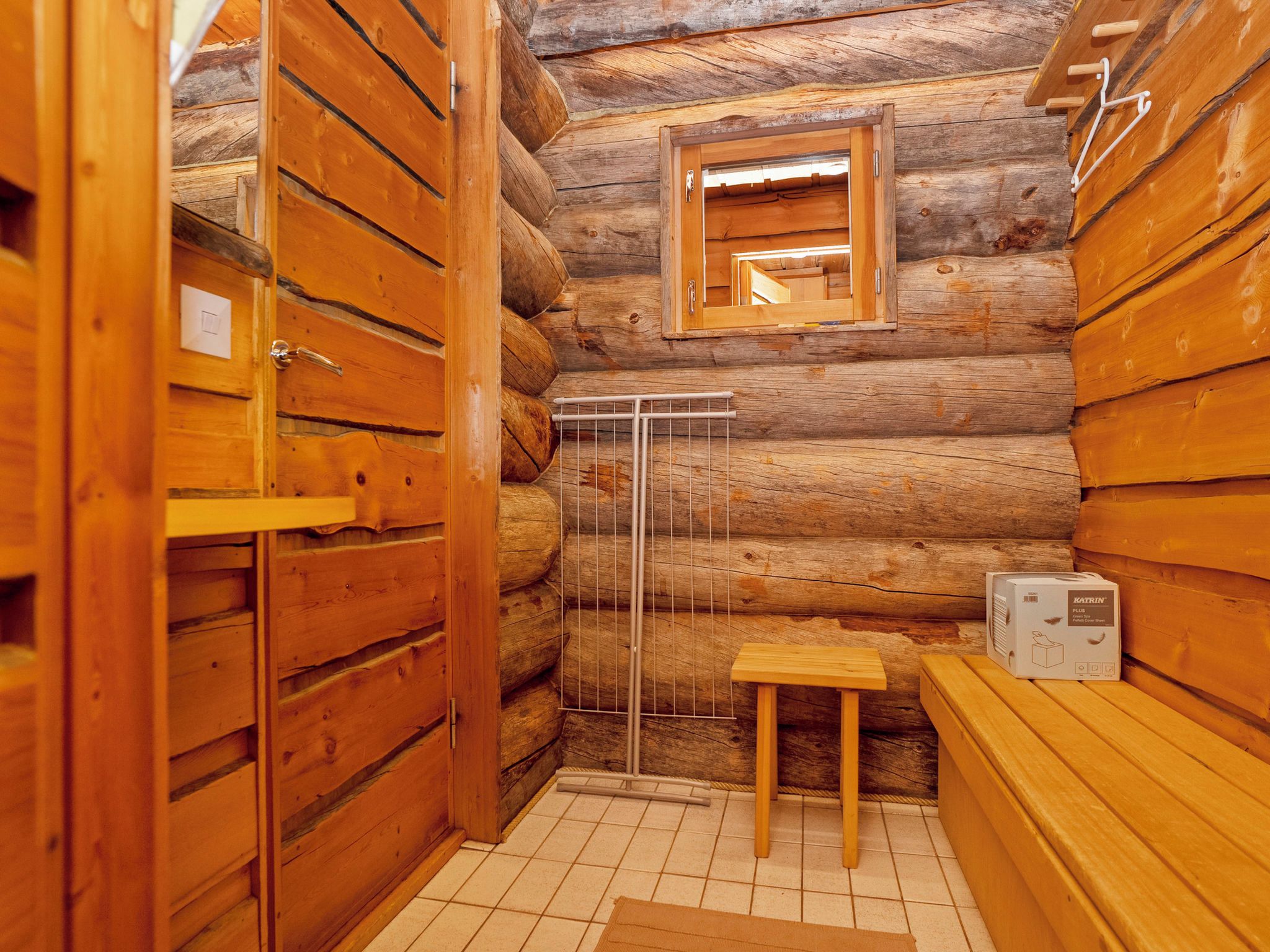 Un baño tipo cabaña de madera con paredes de madera, una ventana pequeña, un perchero y un calentador.