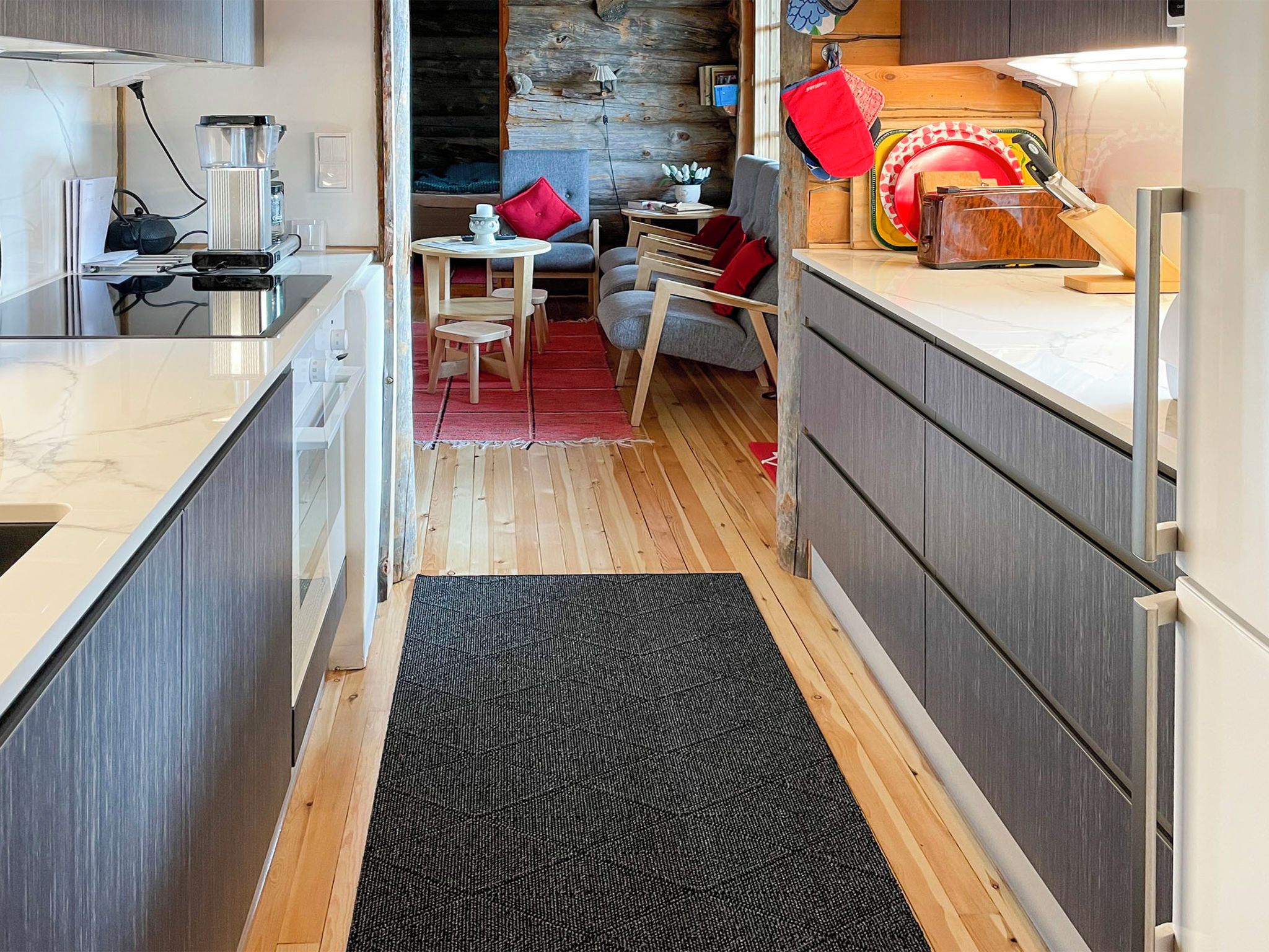 A modern kitchen with wooden flooring, a black rug, and a dining area with a red chair.