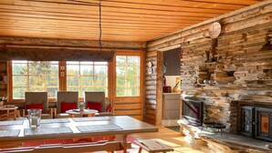 A rustic cabin interior with a wooden dining table, benches, and a stone fireplace.