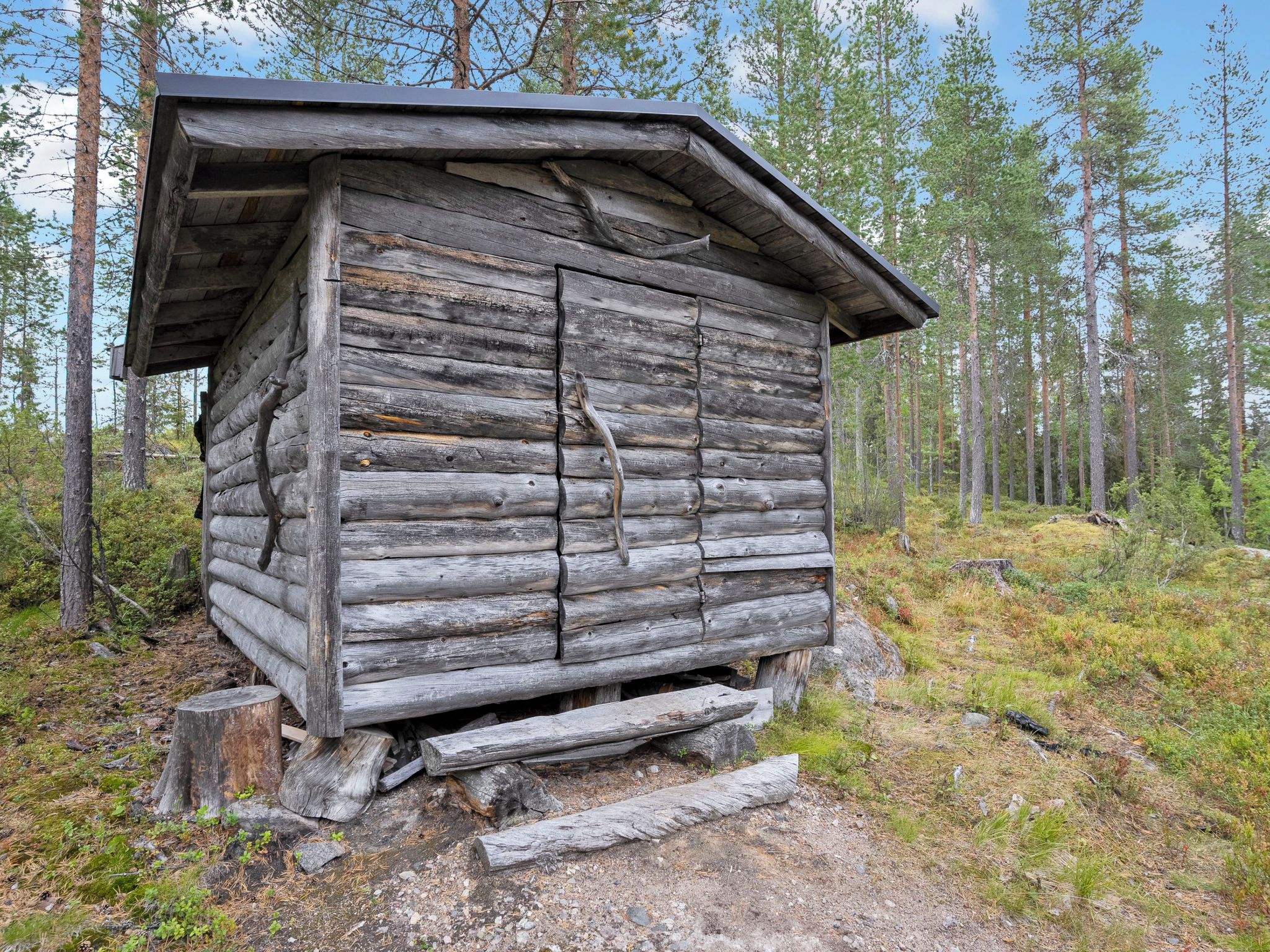 A rustic wooden cabin with a sloped roof, surrounded by a forest.