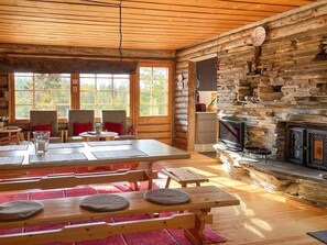L’intérieur d’une cabane en rondins comprend un coin repas, deux chaises, une table, une cheminée et un téléviseur.