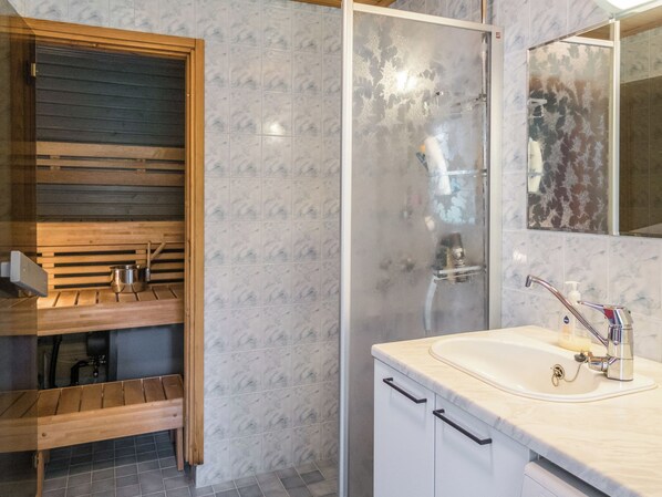 A modern bathroom with a wooden vanity, a glass shower enclosure, and a marble-tiled wall.