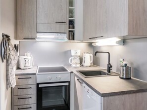 Et lille køkken med indbygget ovn, kaffemaskine og vask.