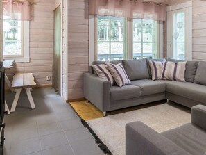 A cozy room with a grey sofa, striped pillows, a small white table, and a large window with a view of trees.