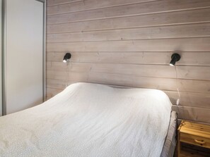 A bed with a white textured cover, a wooden headboard, and two wall-mounted light fixtures.