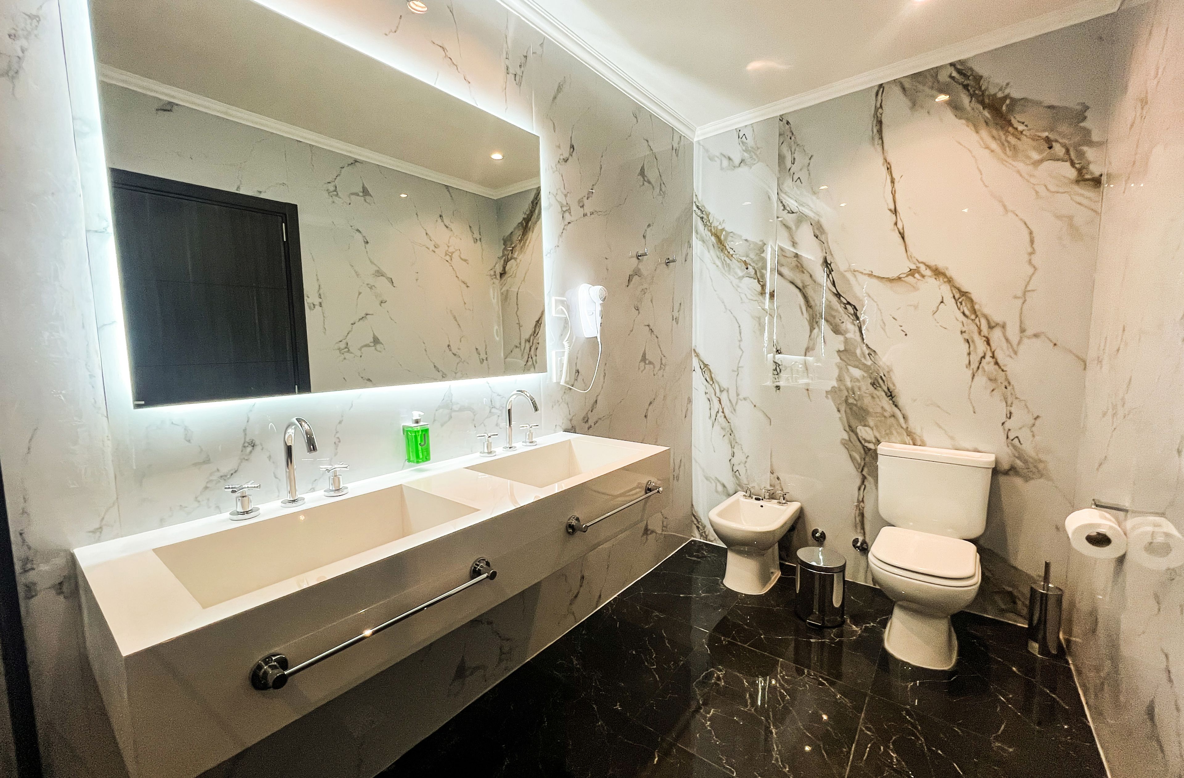 A modern bathroom with a large mirror, a double sink vanity, a bidet, and a toilet.